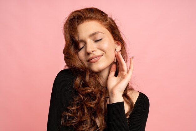 beauty portrait of red head woman posing over pink wall. Wavy hairs. Perfect smile.