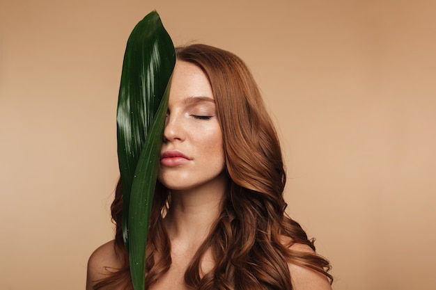Beauty portrait of sensual ginger woman with long hair posing with green leaf