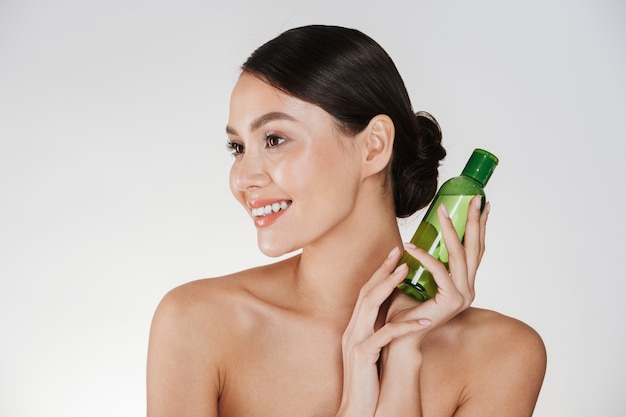 Beauty portrait of smiling brunette woman with soft healthy skin holding lotion for removing makeup, isolated over white