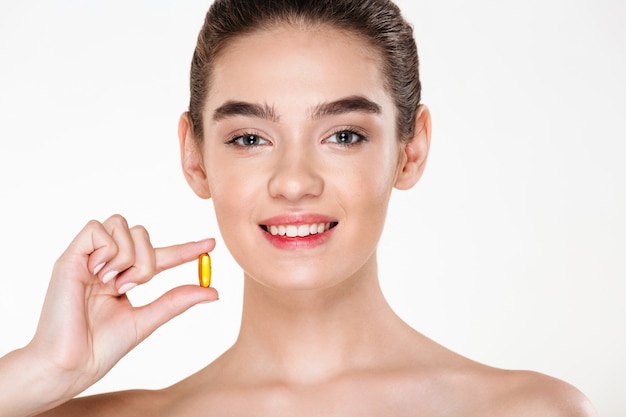 Beauty portrait of smiling healthy woman with dark hair holding capsule meds or vitamin in her hand posing