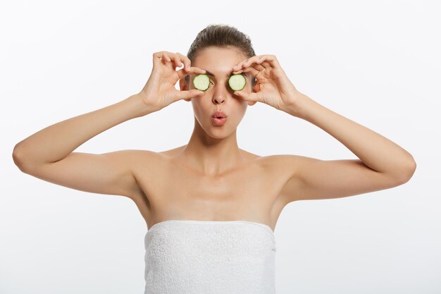 Beauty portrait of smiling woman with towel on head and slice of cucumber in hand isolated on white