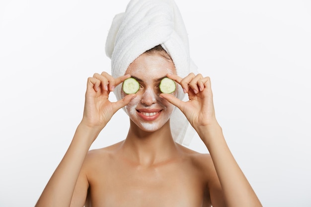 Beauty portrait of smiling woman with towel on head and slice of cucumber in hand isolated on white