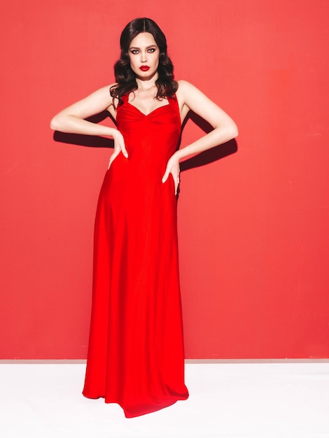 Портрет красоты молодой брюнетки с вечерним макияжем и идеально чистой кожей Сексуальная модель с вьющимися волосами, позирующая в студии с красными яркими натуральными губами, изолированными в модном платье