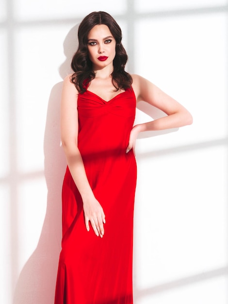 Портрет красоты молодой брюнетки с вечерним макияжем и идеально чистой кожей Сексуальная модель с вьющимися волосами, позирующая в студии с красными яркими натуральными губами, изолированными в модном платье