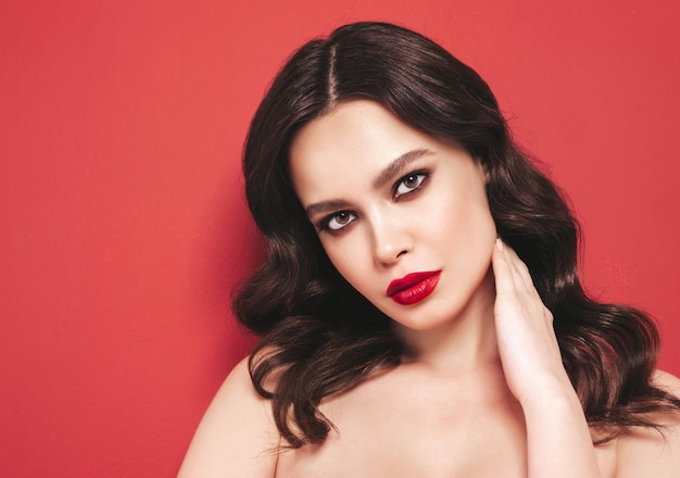 Beauty portrait of young brunette woman with evening makeup and perfect clean skin Sexy model with curly hair posing in studio With red bright natural lips Isolated on red background