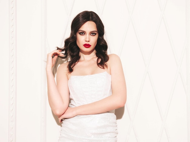 Beauty portrait of young brunette woman with evening makeup and perfect clean skin Sexy model with curly hair posing in studio With red bright natural lips In silver dress