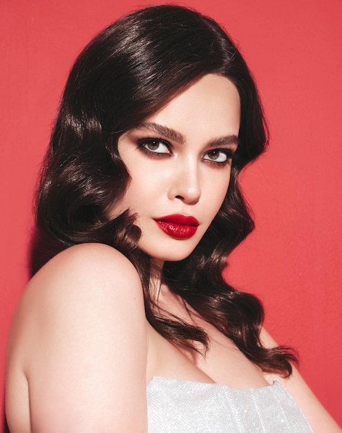 Beauty portrait of young brunette woman with evening makeup and perfect clean skin Sexy model with curly hair posing in studio With red bright natural lips In silver dress