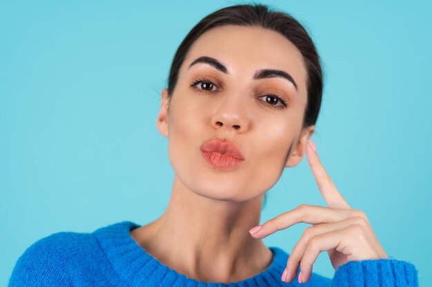 Beauty portrait young woman in a blue knitted sweater and natural daytime makeup, full lips with nude matte lipstick and perfect eyebrows, sends a kiss