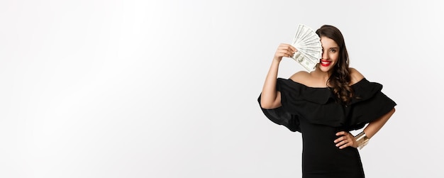 Free photo beauty and shopping concept fashionable woman with red lips showing dollars and smiling standing ove