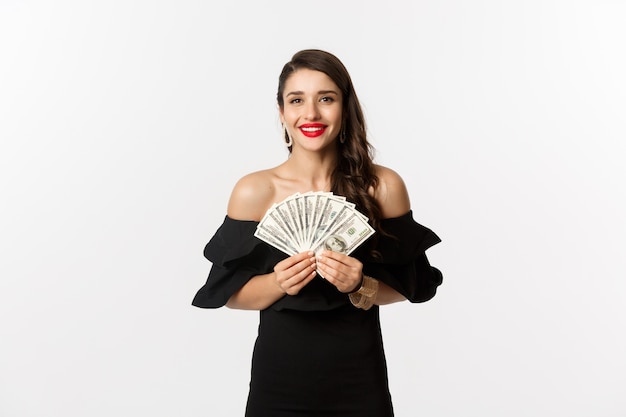 Концепция красоты и покупок. Модная женщина с красными губами, показывая доллары и улыбаясь, стоя на белом фоне с деньгами.
