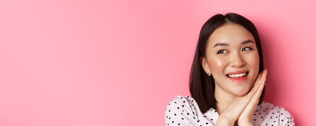 Free photo beauty and skin care concept headshot of adorable and dreamy asian woman looking left smiling and im