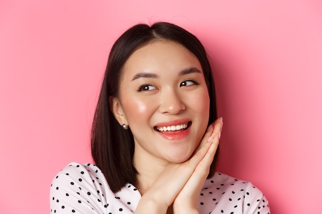 Beauty and skin care concept. headshot of adorable and dreamy asian woman looking left, smiling and imaging, standing against pink background