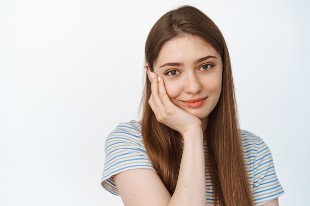 Beauty and skin care. Tender woman gently touching her face and smiling at camera on white