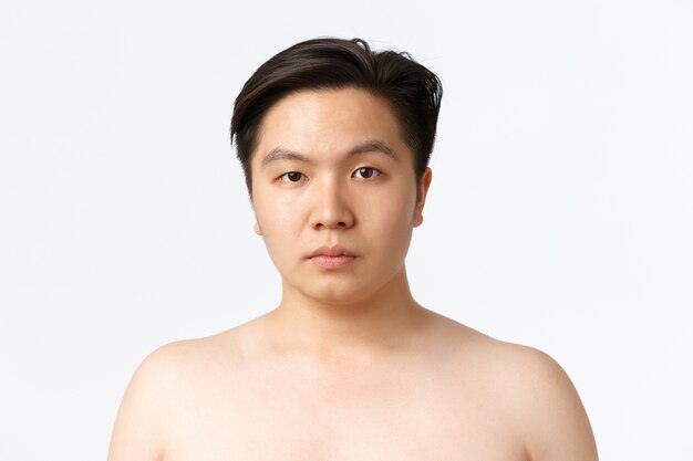 美容、スキンケア、衛生の概念。にきびを起こしやすい肌を持つ若いアジア人のクローズアップ、白い壁の上に裸で立って、皮膚洗浄剤、白い壁を使用した後の前の広告