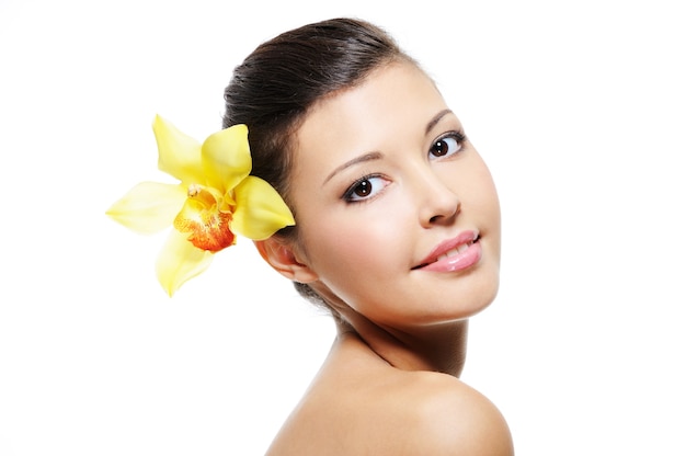 Beauty smiling female face with yellow orchid from her ear - over white