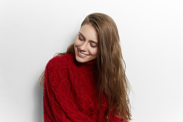 Beauty, style, fashion, clothes and seasons concept. Picture of adorable cute young lady with broad charming smile posing isolated, wearing warm cozy knitted sweater made by her mother