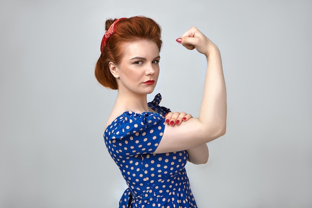 Free photo beauty, style and fashion. power and strength. portrait of serious attractive young woman in vintage stylish clothing, tensing bicep, demonstrating her strong muscles