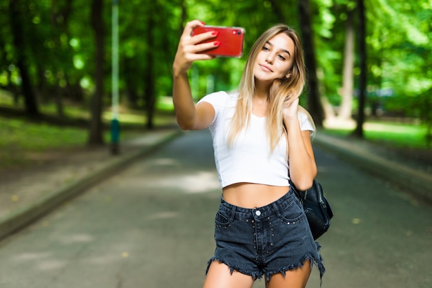 晴れた日に屋外の公園でスマートフォンでselfieを取っている10代の美少女。