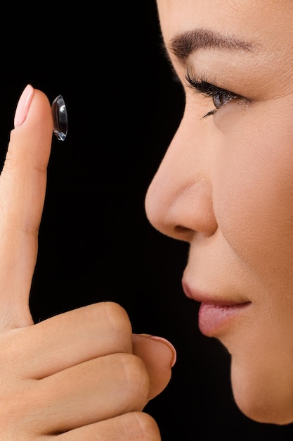 Concetti di bellezza, visione, vista, oftalmologia e persone. profilo del primo piano della donna coreana o asiatica che mette le lenti a contatto in studio.