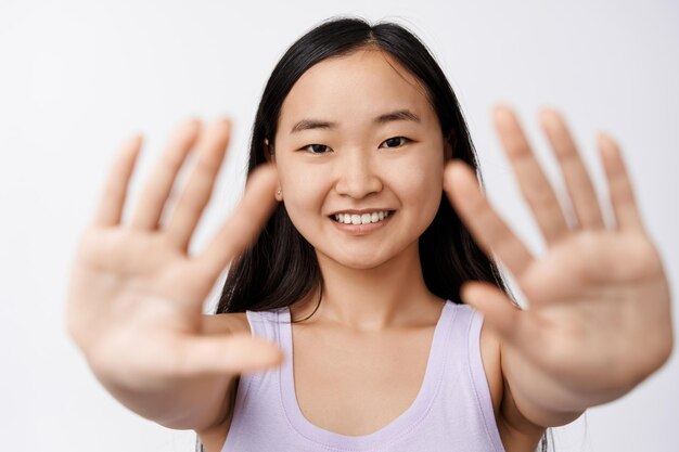 아름다움과 웰빙 행복한 아시아 소녀는 빈 손바닥을 보여주고 카메라 흰색 배경에서 평온한 표정으로 웃는 손을 뻗어
