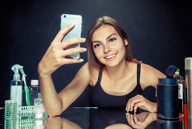 Beauty woman after applying makeup.Beauty woman with makeup. Beautiful girl looking at mobile phone and making selfie photo 