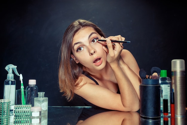 Beauty woman applying makeup. Beautiful girl looking in mirror and applying cosmetic with a brush