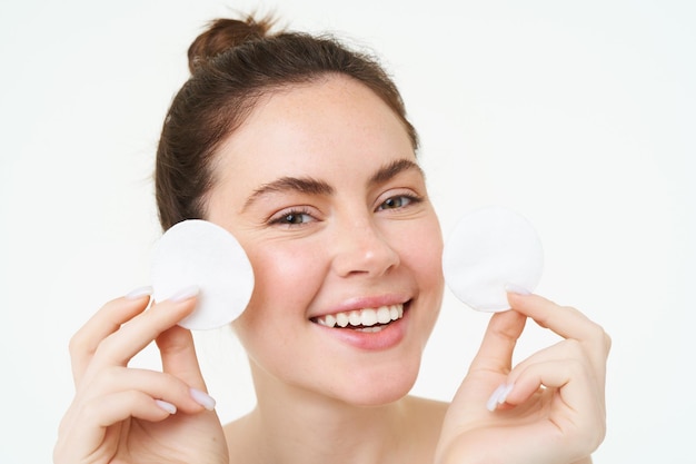 Free photo beauty woman with clear glowing face showing cotton cosmetic pads for makeup removal cleansing her