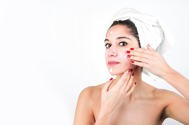 Beauty young woman applying cream on the face isolated over white backdrop