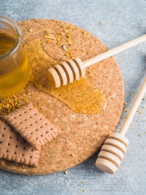 Bee pollens; honey; biscuits and wooden dipper on cork coaster
