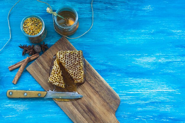 Bee pollens jar; spices and honeycomb piece with knife against blue textured background