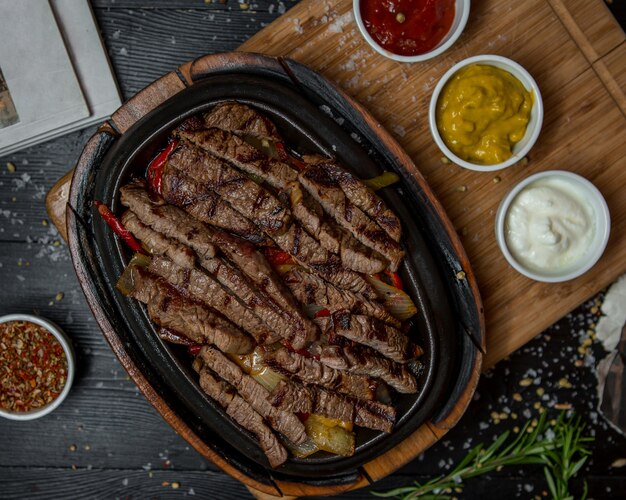 Beef fajitas with three kind of sauces on a wooden board