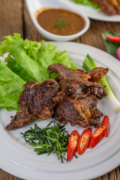 Beef fried Thai food on a white plate with spring onion, kaffir lime leaves, chilies, salad and chili paste in a cup.