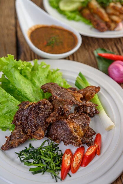 Beef fried Thai food on a white plate with spring onion, kaffir lime leaves, chilies, salad and chili paste in a cup.