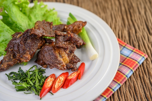 Beef fried Thai food on a white plate with spring onion, kaffir lime leaves, chilies, salad and chili paste in a cup.