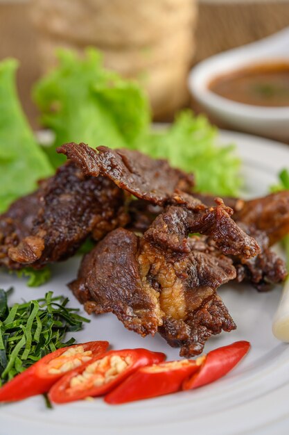 Beef fried Thai food on a white plate with spring onion, kaffir lime leaves, chilies, salad and chili paste in a cup.