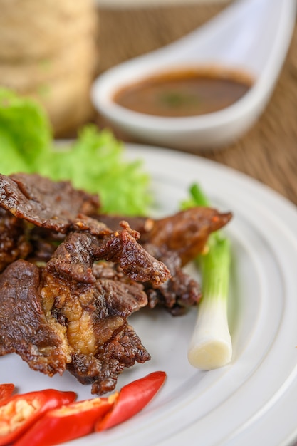 Beef fried Thai food on a white plate with spring onion, kaffir lime leaves, chilies, salad and chili paste in a cup.