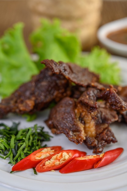 Beef fried Thai food on a white plate with spring onion, kaffir lime leaves, chilies, salad and chili paste in a cup.