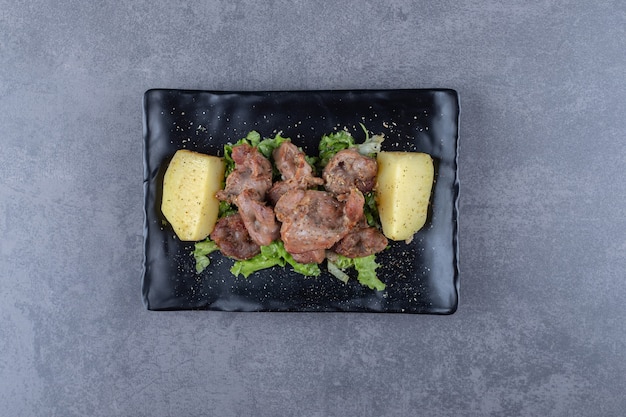 Beef kebab and boiled potatoes on black plate.