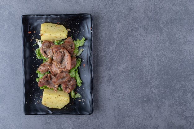 검은 접시에 쇠고기 케밥과 삶은 감자.