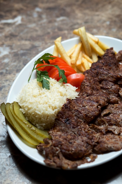 Beef kebab plate with french fries, cucumber pickles, rice and tomato