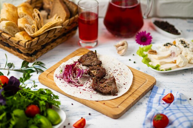 Beef meat kebab with onions, sumakh and lavash on a wooden plate served with wine and vegetables 