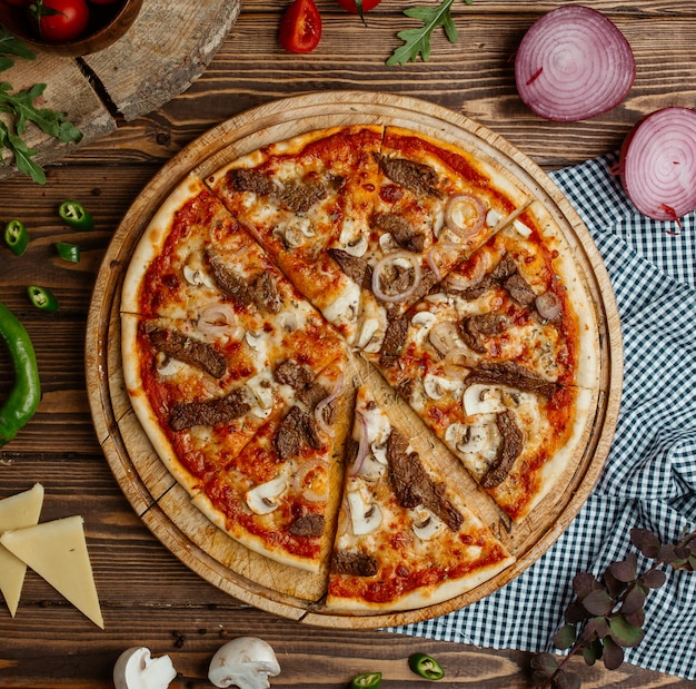 beef-mushroom pizza with onion and cheese on wooden plate