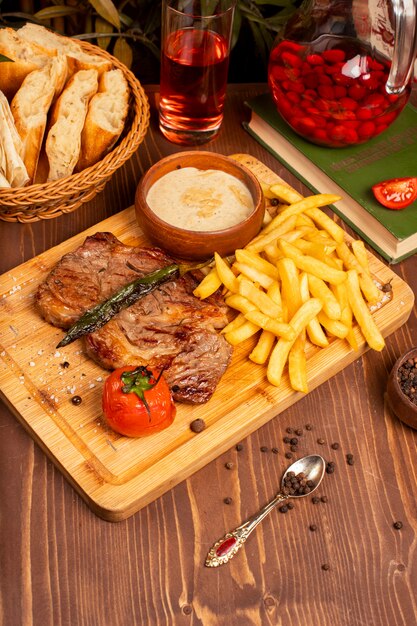 Beef steak with french fries, sour cream mayonnaise sauce and herbs on wooden plate. 