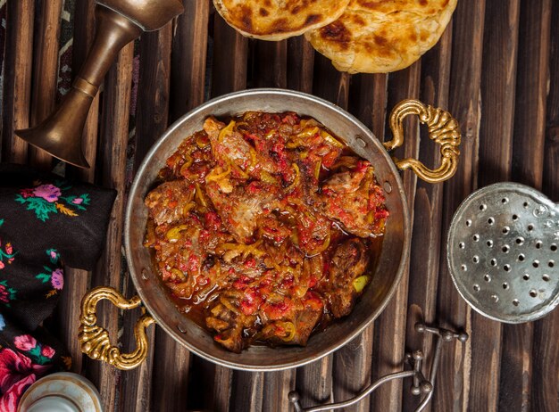 Beef stew in tomato sauce inside copper pan.