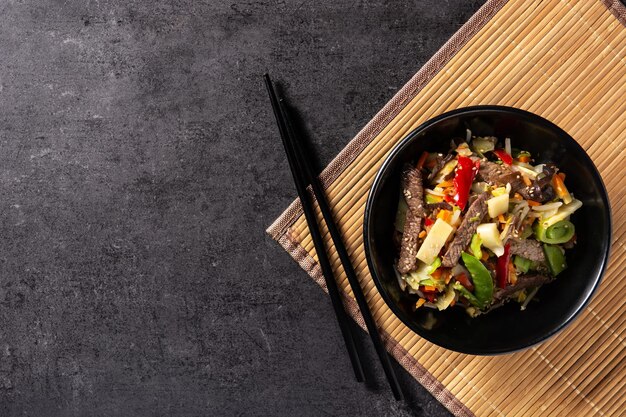 黒のスレートの背景に黒のボウルに牛肉、野菜、ゴマ