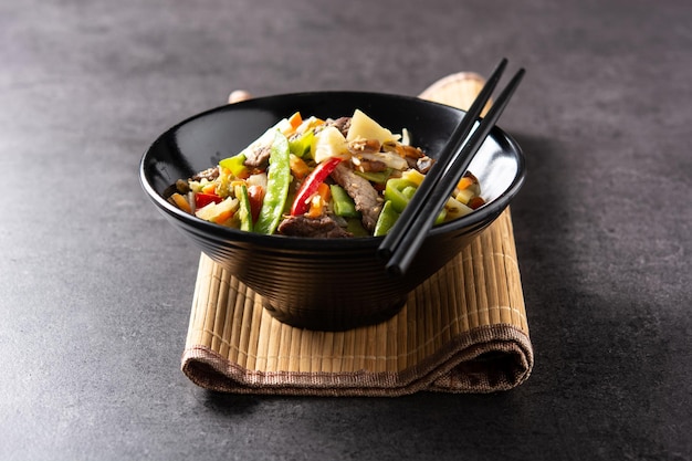 Beef, vegetables and sesame seeds in black bowl on black slate background