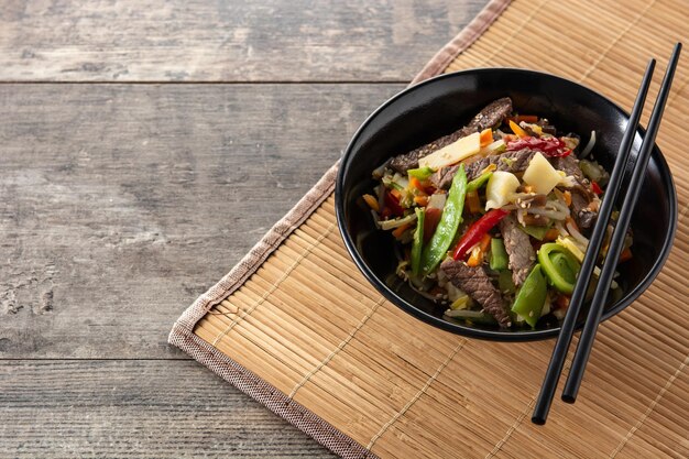 Beef, vegetables and sesame seeds in black bowl on wooden table