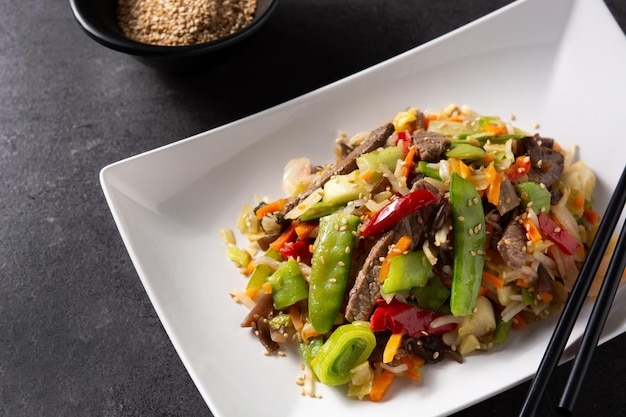 Beef, vegetables and sesame seeds in white plate on black background