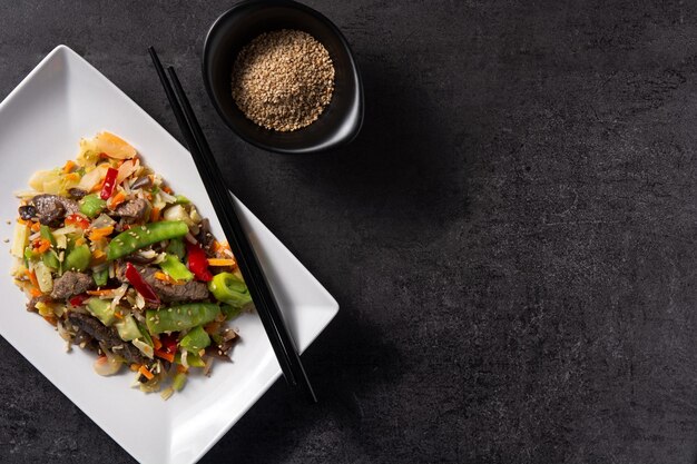 Beef vegetables and sesame seeds in white plate on black background