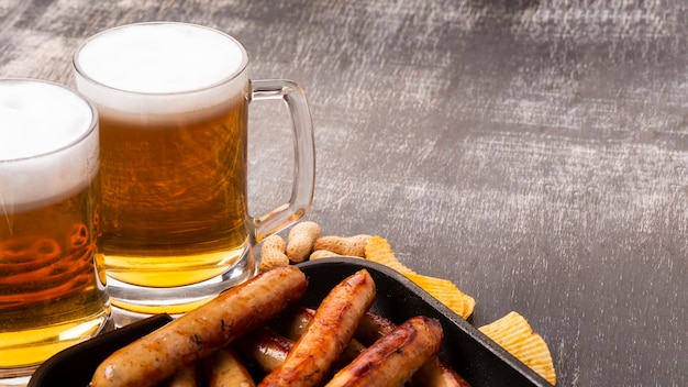 Beer mugs and sausages on dark background